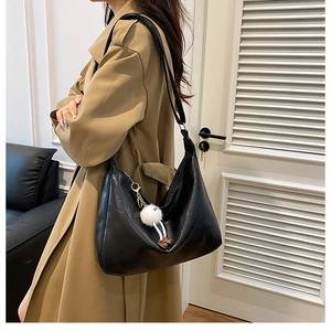Nahaufnahme einer großen schwarzen Hobo-Tasche mit einem süßen weißen Plüsch-Anhänger