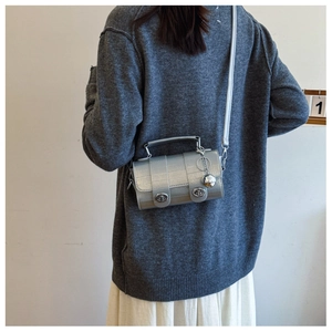 Detail of silver cylindrical crossbody bag with dual metal locks and spherical charm