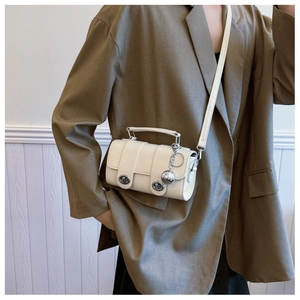 Detail of minimalist cream crossbody bag with crocodile texture and silver ball pendant