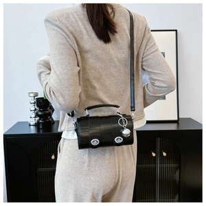 Detail of a black cylindrical crossbody bag featuring silver turn-locks and metal ball charm