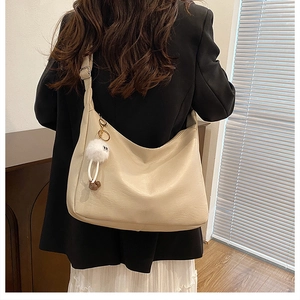 Große beige Hobo-Tasche mit flauschigem Anhänger, getragen von einem Modell im Raum