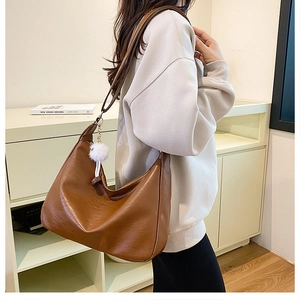 Detail view of brown leather hobo shoulder bag with a white fluffy pompom charm pendant