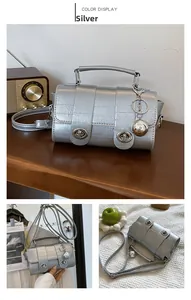 Detail of silver crossbody bag featuring dual twist locks and decorative metal ball