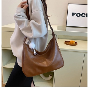 Caramel brown large hobo bag with a white fuzzy pom-pom charm shown in a lifestyle setting
