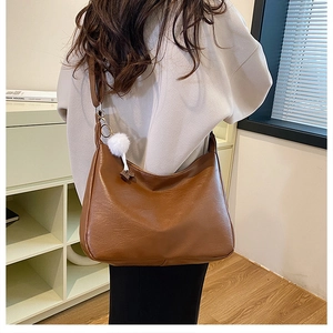 Detailed view of caramel brown large hobo bag with a white plush pompom charm