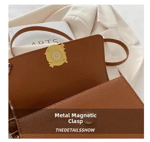 Close-up of golden vintage magnetic snap and litchi grain leather on a brown handbag