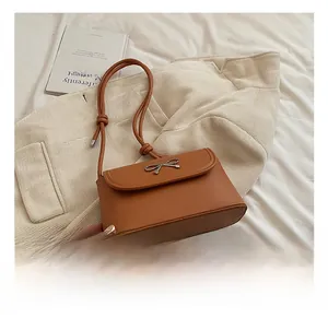 Detail of tan leather crossbody bag featuring metal bow hardware and knotted shoulder strap