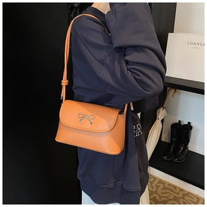 Close-up of orange crossbody bag featuring a silver bow metal clasp and knotted strap detail