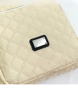 Close-up of beige quilted fabric and silver metal logo on a large capacity shoulder bag