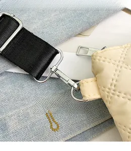 Detailed close-up of the silver metal spring hook and beige quilted fabric strap connection