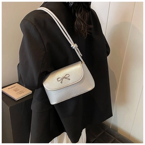 Detail of silver textured crossbody bag with metal bow and adjustable shoulder strap