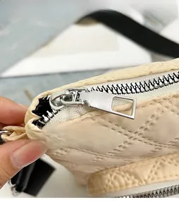 Detail view of the beige quilted nylon bag featuring a smooth silver metal zipper puller