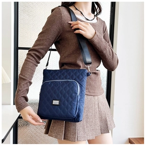 Detailed shot of dark blue quilted nylon crossbody bag with adjustable wide strap and zipper