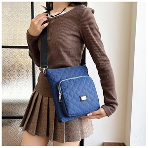Detail of dark blue quilted nylon crossbody bag with adjustable wide strap and metal hardware