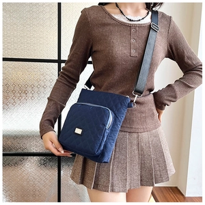 Detail of navy blue quilted crossbody bag with adjustable strap and front zipper pocket