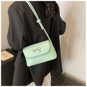 Detail shot of a mint green underarm bag with a silver bow decoration worn with black blazer