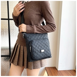 Close-up of black quilted nylon crossbody bag featuring silver zippers and logo plate detail
