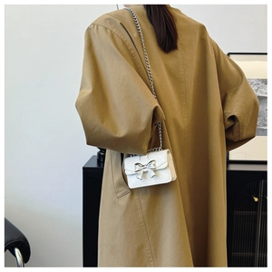 Mini sac carré blanc avec nœud argenté porté sur un mannequin en trench-coat kaki