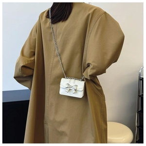 Detailed back view of a white mini crossbody bag with silver bow and chain on a trench coat