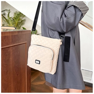 Detail of beige quilted crossbody bag featuring a front zipper pocket and adjustable strap