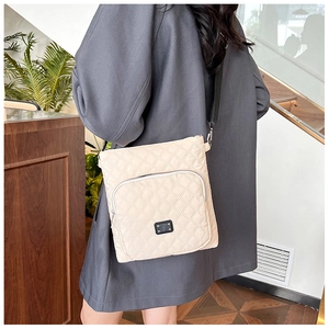 Detail of beige quilted nylon crossbody bag with black adjustable strap and brand metal plate