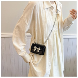 Detail shot of mini black chain bag with silver bow on beige textured clothing