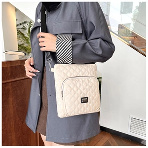 Close-up of beige quilted crossbody bag with metal logo and adjustable black strap