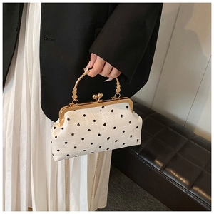 Close-up of beige polka dot shell bag with gold metal handle and chain strap detailing