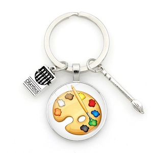 Artistic silver paint palette keychain with paintbrush and crayons charms on white background