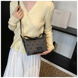 Close-up of gray polka dot shoulder bag with bow details and brand label on a model