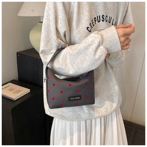 Detail of grey fabric pea bag with red polka dots and a black handle held by a model