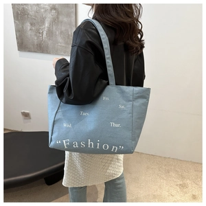 Detail of light blue denim tote bag with Fashion print shown from a side view on shoulder