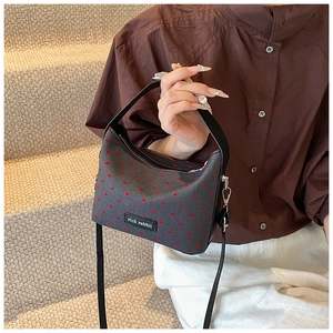 Detail view of dark grey handbag featuring red heart patterns and leather branding logo
