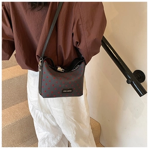Close-up of dark grey crossbody bag featuring red heart patterns and adjustable strap