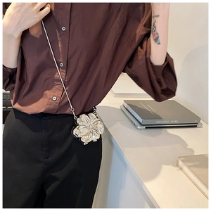 Detail of a 3D silver flower crossbody bag with chain worn by a female model