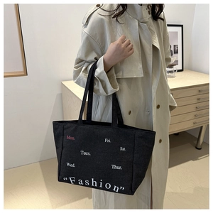 Detailed view of black canvas tote bag with white fashion print on elegant beige coat