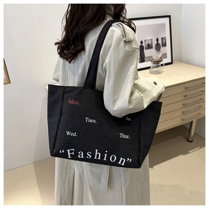 Detail of black canvas tote bag with fashion typography on shoulder of a model