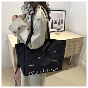 Detail of black canvas tote bag with daily week print worn with a beige trench coat