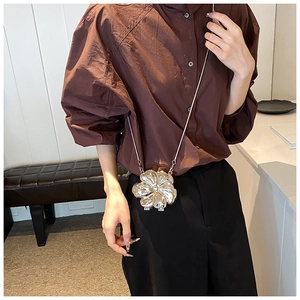 Detail shot of silver flower shaped metal clutch bag with a slim metallic chain strap
