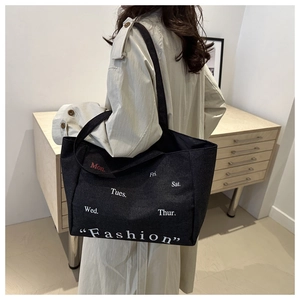 Detail of large black denim tote bag featuring white and red fashion text and strap