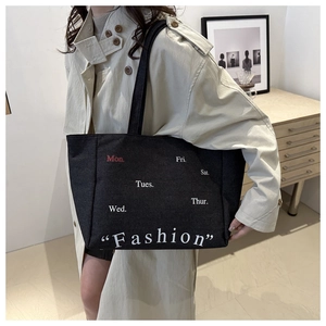 Detail of a black denim tote bag featuring weekday prints and a large capacity for commute