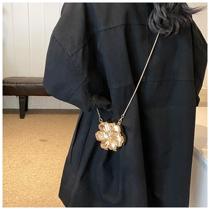Detail of flower shaped gold evening bag with thin chain strap on a black outfit