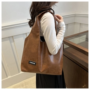 Close-up of a brown PU leather tote bag with a fashion label and wide shoulder strap