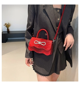 Detail of red crocodile texture handbag with sparkling rhinestone bow and leather strap