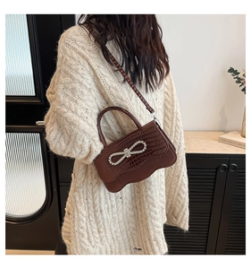 Detail of dark brown faux crocodile handbag with rhinestone bow on beige knit sweater