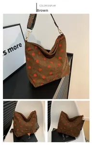 Detail of brown corduroy bucket bag featuring red strawberry prints and ethnic woven strap