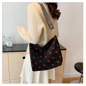 Detail of strawberry print corduroy bucket bag with ethnic geometric strap worn by model