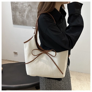 Detail view of cream canvas tote bag with brown leather trim and bow knot accessory