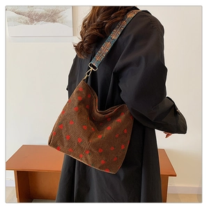 Detail of strawberry corduroy tote with ethnic embroidered shoulder strap worn by model