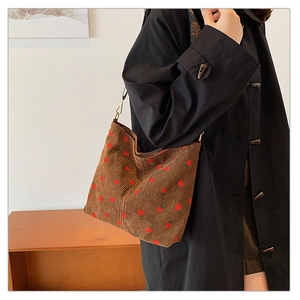 Detailed texture of brown corduroy shoulder bag with embroidered red strawberry patterns